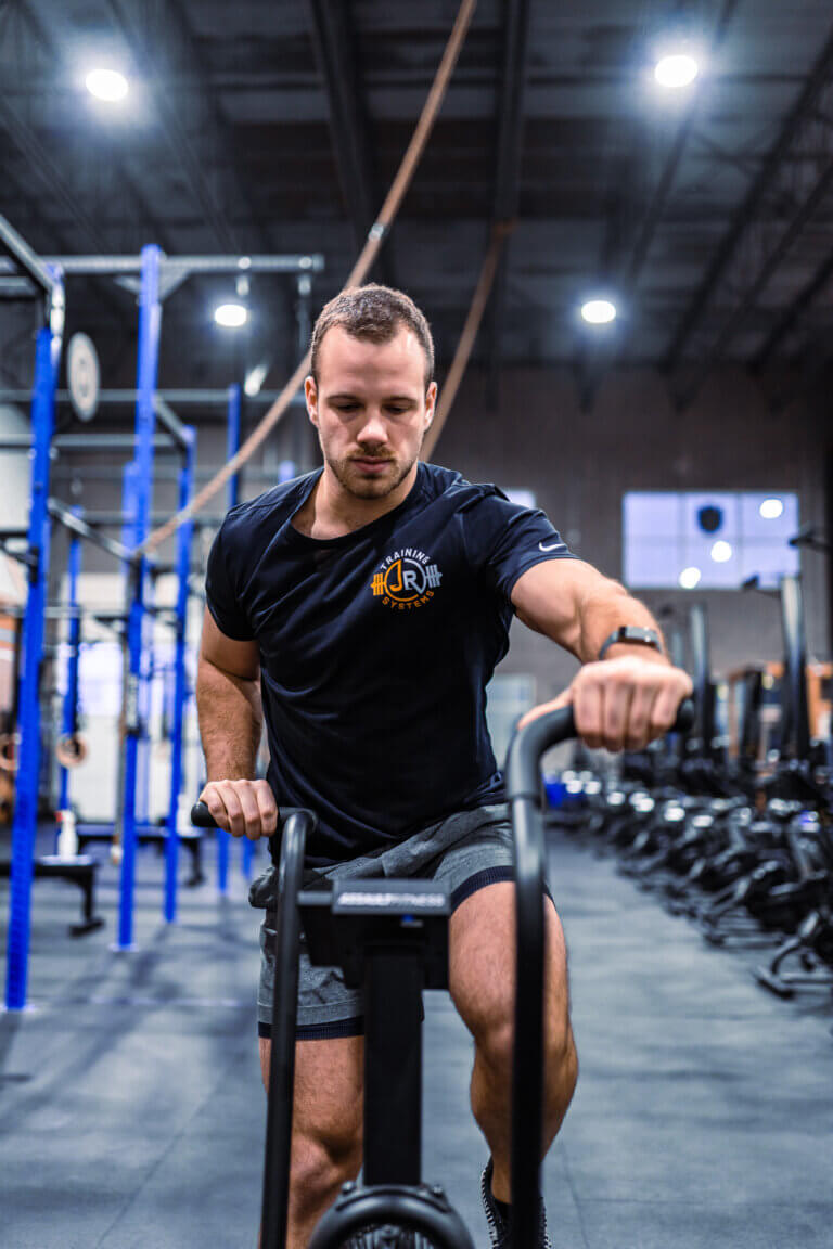 Personal trainer in a black shirt performing moderate-intensity Zone 2 cardio on an assault bike