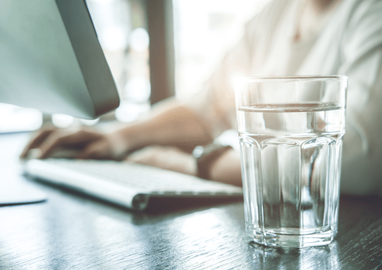 A glass of refreshing water sits on a desk beside a person immersed in work, creating a productive and hydrating workspace.