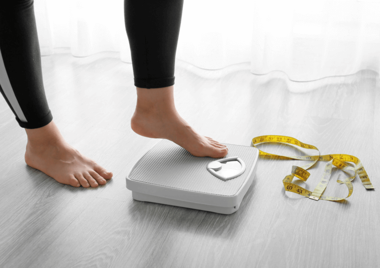 "Woman standing on a white bathroom scale, with a measuring tape nearby, symbolizing health monitoring and weight management.